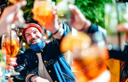 Preview: Happy guy toasting fancy drinks at night bar with open mask