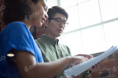 Preview: Diverse male and female colleague looking at paperwork and discussing standing in office