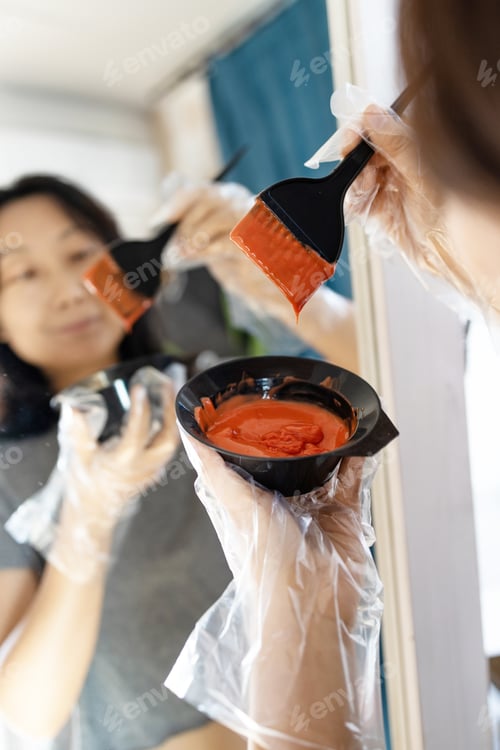 Preview: Hair coloring at home. Middle aged woman dyes her hair black with a brush. Asian woman dyes her dark