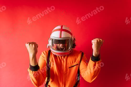 Preview: Astronaut with a helmet and an orange space suit with fists raised in sign of victory