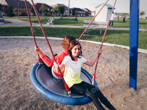 Preview: Two young girls having fun on a swing at a playground, suburbs