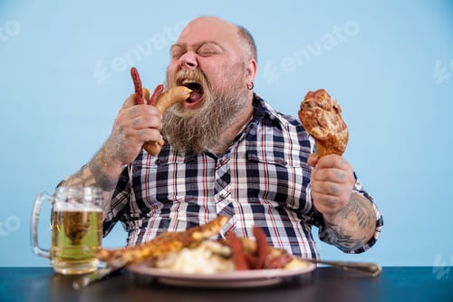 Preview: Hungry plus size man eats sausages at table with rich food and mug of beer