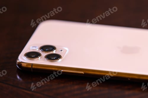 Preview: iPhone11 Pro Max in gold with focus on the triple lens. Placed on a mahogany wood table.