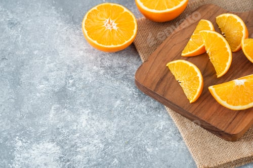 Preview: A wooden board full of juicy slices of orange fruit on stone background
