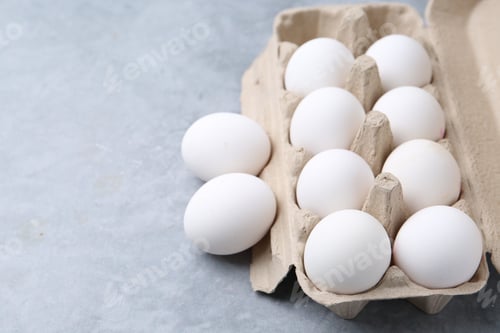 Preview: Raw chicken eggs in egg carton on grey table, closeup. Space for text