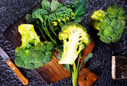 Preview: fresh green broccoli on wooden cutting board with knife. Broccoli cabbage leaves. dark background.