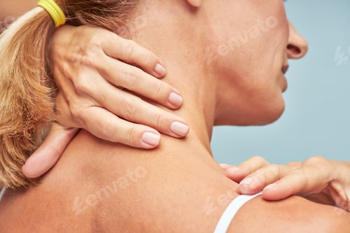 Preview: Rear view of a mature woman touching her neck and shoulder while standing against blue background