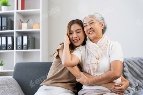 Preview: Asian grandmother and adult granddaughter embracing on sofa
