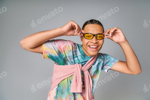 Preview: cheerful african american man in sunglasses and tie-dye t-shirt smiling at camera on grey