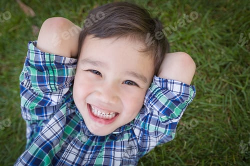Preview: Mixed Race Chinese and Caucasian Young Boy Relaxing On His Back Outside On The Grass