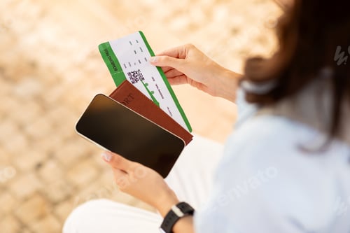 Preview: Millennial european woman with passport and ticket looks at smartphone with empty screen