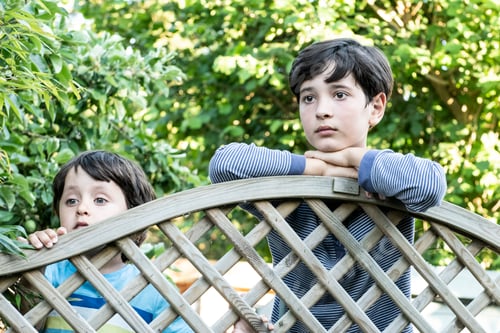 Preview: Two boys leaning on a wooden lattice fence outdoors.