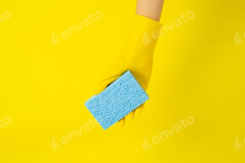 Preview: Gloved Hand Holding Blue Sponge on Yellow Background
