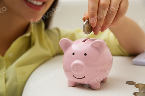 Preview: Woman putting coin into piggy bank indoors, closeup. Money savings