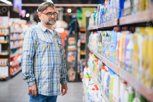 Preview: Portrait of focused man buying household chemicals in supermarket, reading labels on bottles