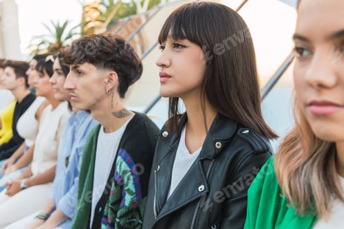 Preview: Serious young ethnic woman sitting with diverse friends in daylight on building roof