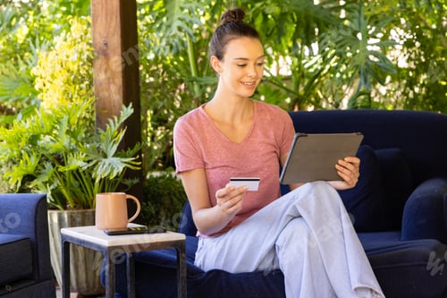 Preview: Shopping online, young woman holding credit card and using tablet on couch