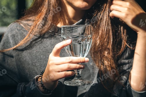 Preview: A woman in a cafe holds a glass of water in her hand.