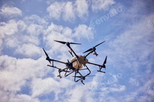 Preview: Photo of an agro drone in the air, flying above fields, has an automatic sprayer.