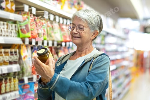 Preview: Portrait smiling senior woman making purchases in the supermarket selecting some jam
