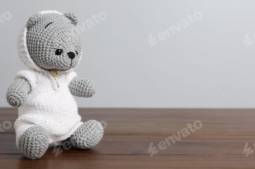 Preview: Cute knitted toy bear on wooden table against light background. Space for text