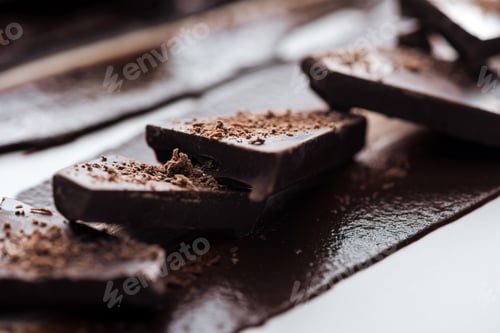 Preview: Selective focus of pieces of chocolate bar with cocoa powder and melted chocolate