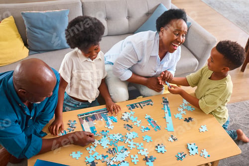 Preview: Grandparents With Grandchildren Indoors Sitting Around Table At Home Doing Jigsaw Puzzle Together