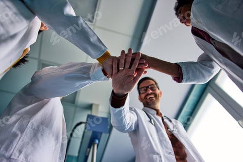 Preview: A team of smiling female and male doctors folded hands together in the hospital.