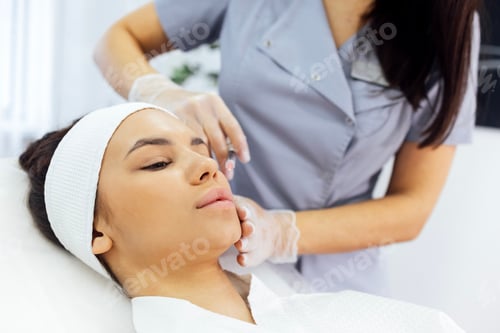 Preview: Female cosmetologist in transparent gloves makes an injection in the lower jaw of her client