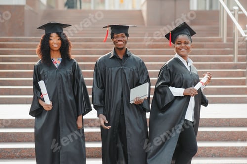 Preview: group of happy international students in mortar boards and bachelor gowns with diplomas