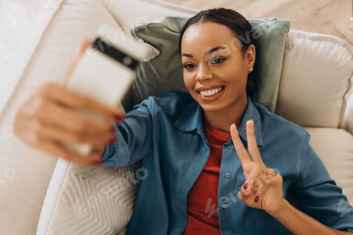 Preview: Happy African American woman holding mobile phone, using mobile app, influencer recoding video