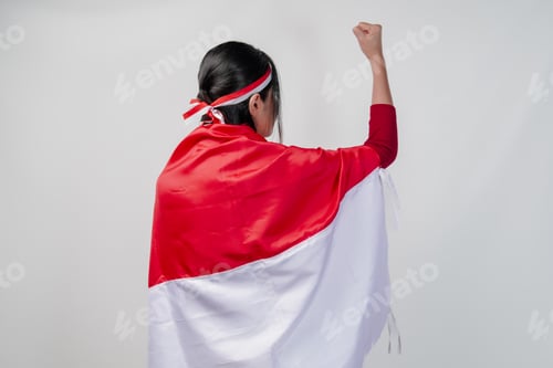 Preview: Back portrait of Asian woman covering herself with Indonesia flag and holding her fist up.