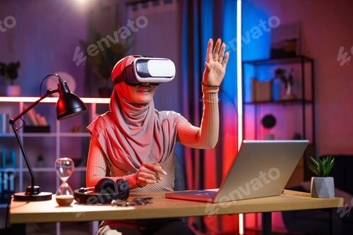 Preview: Arab muslim woman in headscarf, using 3D augmented reality goggles at home in the evening