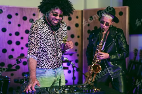 Preview: Young happy people playing music with dj mixer and saxophone in house studio