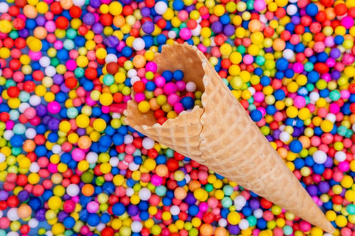 Preview: An empty waffle cone with scattered multicolored round candies, dragees. Children's sweets.
