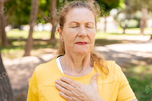 Preview: Senior woman meditating in park, eyes closed, hand on chest, mindful and peaceful