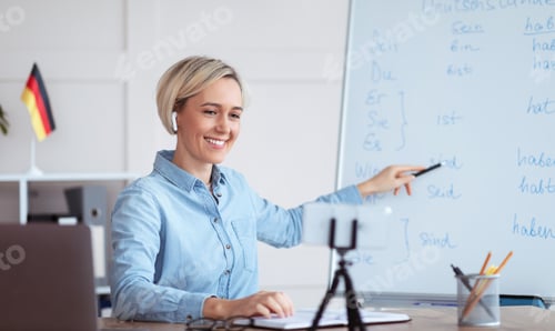 Preview: Online languages school. Female tutor giving German lesson on internet, using smartphone, explaining