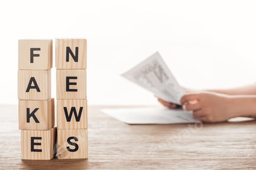 Preview: cropped image of journalist reading newspaper, wooden cubes with words fake news at wooden table