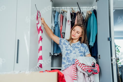 Preview: Woman selecting clothes from her wardrobe for donating to a Charity shop. Decluttering