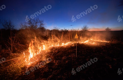 Preview: Burning dry grass and warning sign in field at night