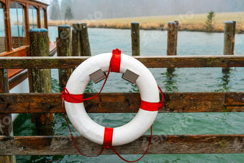 Preview: White lifebuoy with red stripes on wooden pier near boat on water