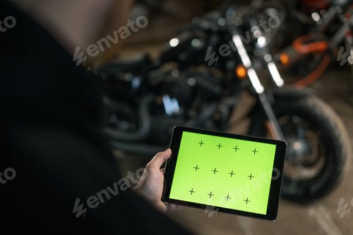 Preview: motorcycle workshop Biker mechanic in garage standing near motorcycle holding green screen tablet