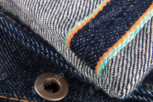 Preview: Close up of jeans fragment with button. Denim texture. Selvage.