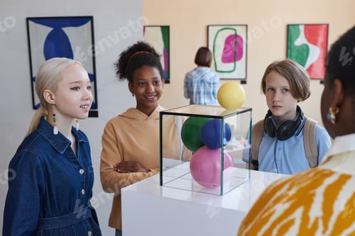 Preview: Diverse group of smiling teenagers listening to tour guide in museum