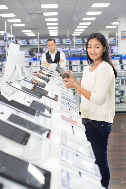 Preview: Portrait of young female shopper browsing digital tablets in electronics store