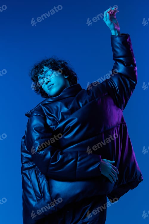 Preview: Man in winter jacket model poses and dances, hipster lifestyle, portrait blue background, mixed neon