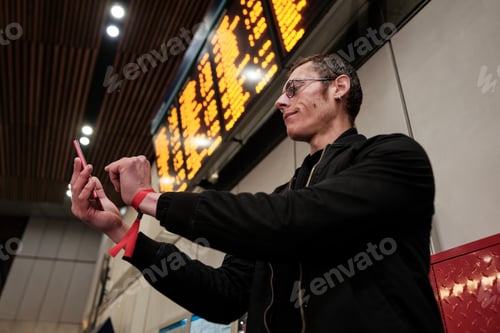 Preview: Young man photographing train schedule information board with smartphone