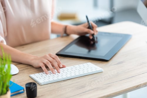Preview: cropped image of female freelancer drawing on graphic tablet at table with computer in home office