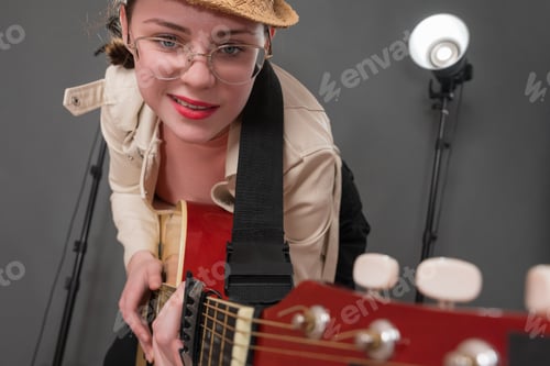 Preview: Cheerful female guitarist with glasses and grin on face is holding guitar and pointing it at camera