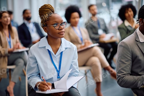 Preview: Young black businesswoman taking notes while attending an education event in board room.